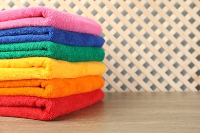 Photo of Colorful fresh terry towels on wooden table, closeup. Space for text