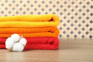 Photo of Colorful fresh terry towels and cotton flower on wooden table, closeup