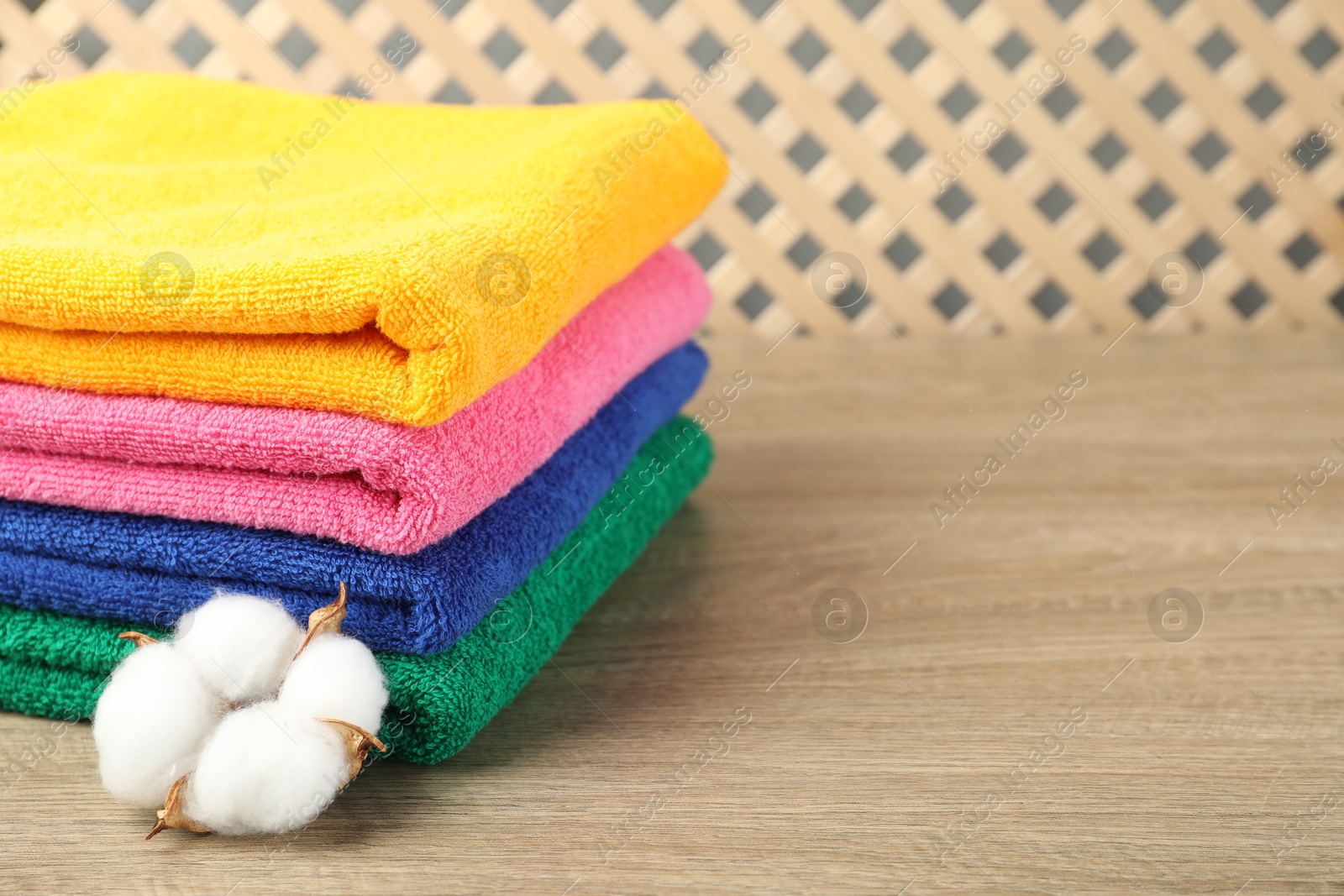Photo of Colorful fresh terry towels and cotton flower on wooden table, closeup. Space for text