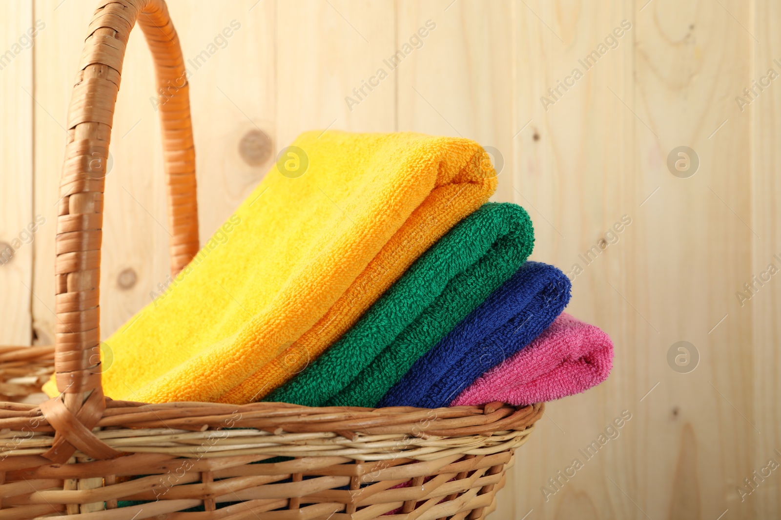 Photo of Colorful fresh terry towels in basket on wooden background, closeup