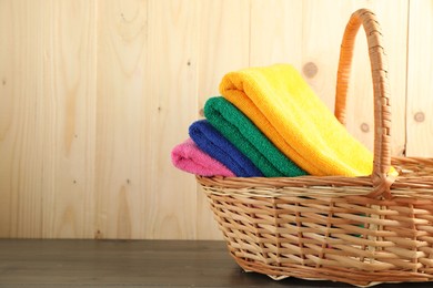 Photo of Colorful fresh terry towels in basket on wooden table, closeup. Space for text
