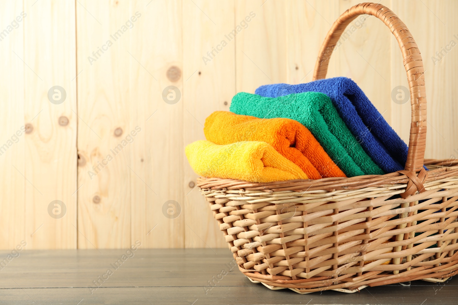 Photo of Colorful fresh terry towels in basket on wooden table, closeup. Space for text