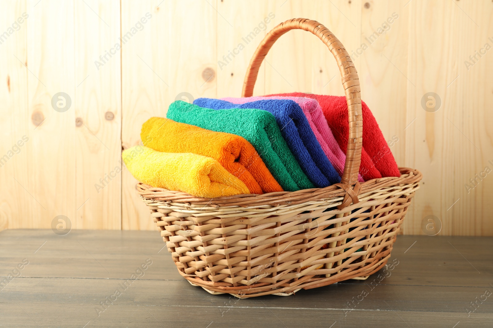 Photo of Colorful fresh terry towels in basket on wooden table