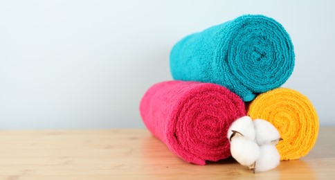 Photo of Colorful fresh terry towels and cotton flower on wooden table, closeup. Space for text