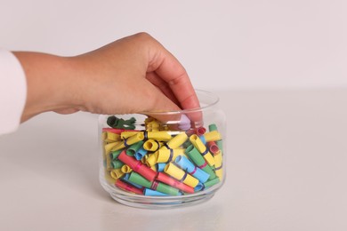 Photo of Woman taking color paper piece from glass jar at white table, closeup