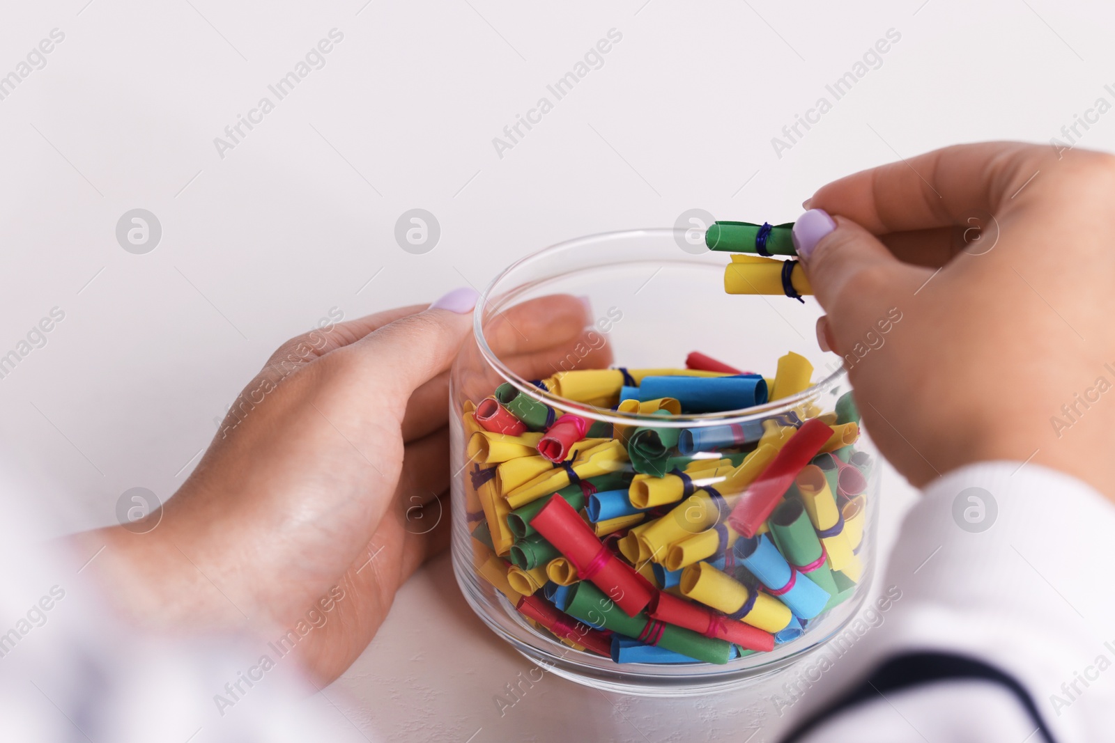 Woman with glass jar of colorful paper pieces at white table, closeup Photo of Woman with glass jar of colorful paper pieces at white table, closeup