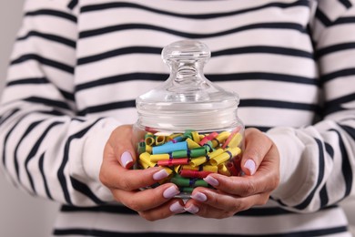 Photo of Woman holding glass jar with colorful paper pieces on light background, closeup