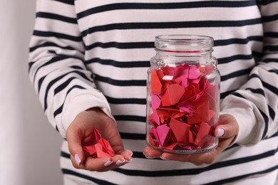 Photo of Woman holding glass jar with colorful paper pieces on light background, closeup