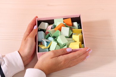Photo of Woman with box of color paper pieces at white wooden table, closeup