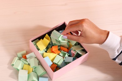 Photo of Woman taking color paper piece from box at white wooden table, closeup
