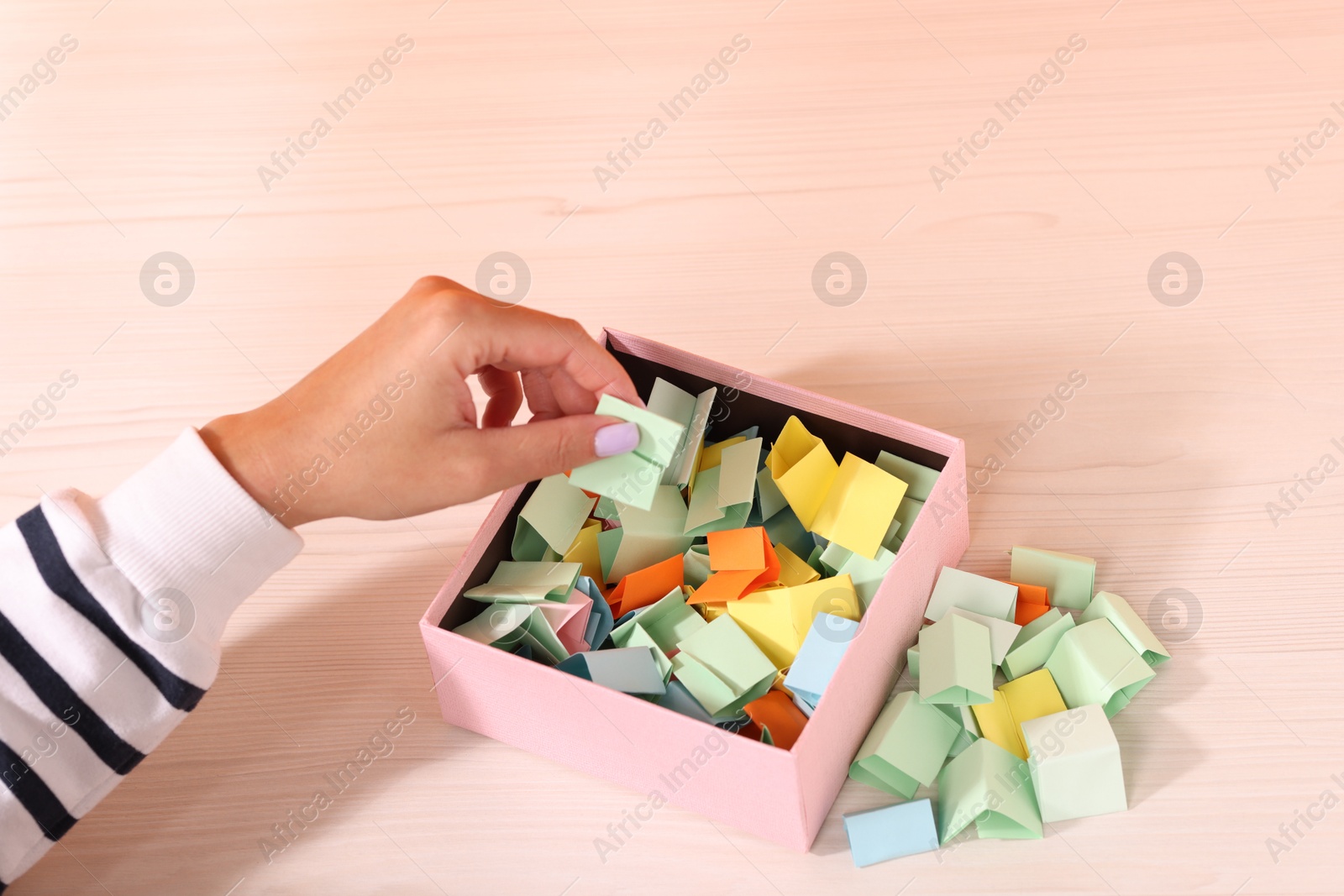 Woman taking color paper piece from box at white wooden table, closeup Photo of Woman taking color paper piece from box at white wooden table, closeup
