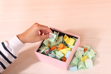 Photo of Woman taking color paper piece from box at white wooden table, closeup
