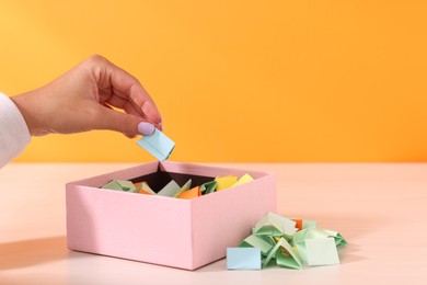 Photo of Woman taking color paper piece from box at white wooden table, closeup