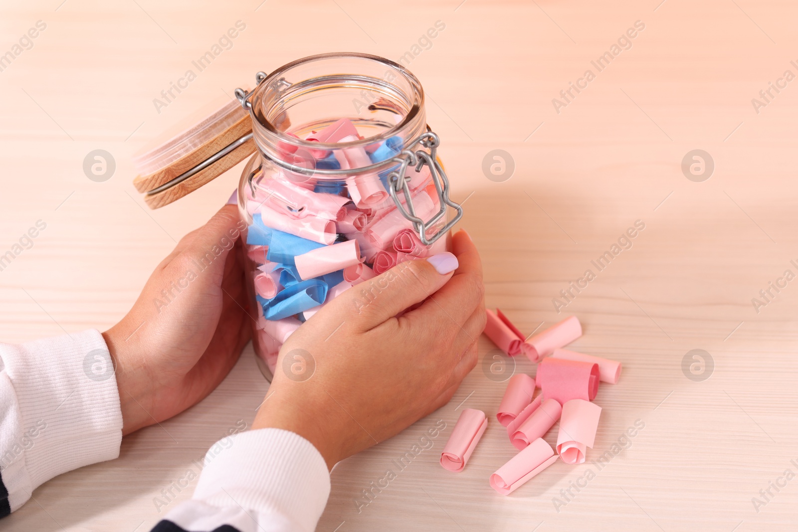 Woman with glass jar of color paper pieces at white wooden table, closeup Photo of Woman with glass jar of color paper pieces at white wooden table, closeup