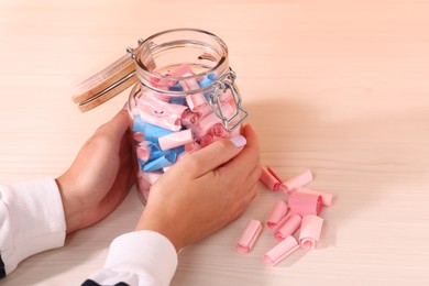 Photo of Woman with glass jar of color paper pieces at white wooden table, closeup