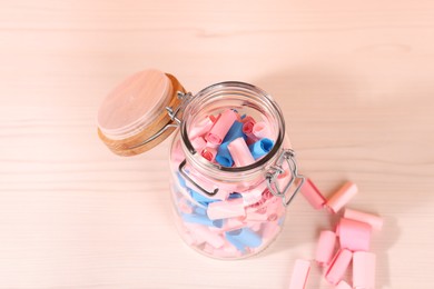 Photo of Color paper pieces in glass jar on white wooden table, above view