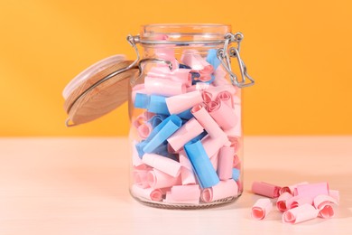 Photo of Color paper pieces in glass jar on white wooden table, closeup