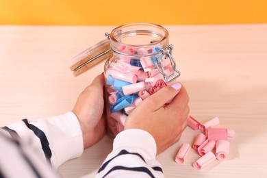 Photo of Woman with glass jar of color paper pieces at white wooden table, closeup