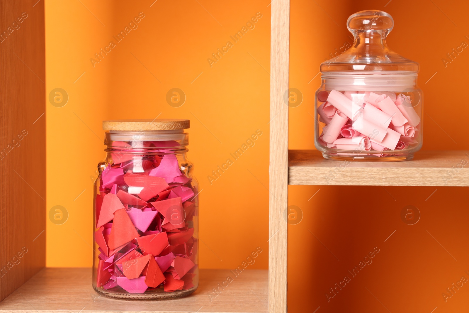 Color paper pieces in glass jars against orange background Photo of Color paper pieces in glass jars against orange background
