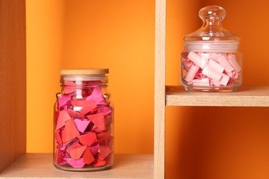 Photo of Color paper pieces in glass jars against orange background