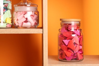 Photo of Color paper pieces in glass jars against orange background