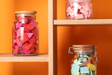 Photo of Color paper pieces in glass jars against orange background