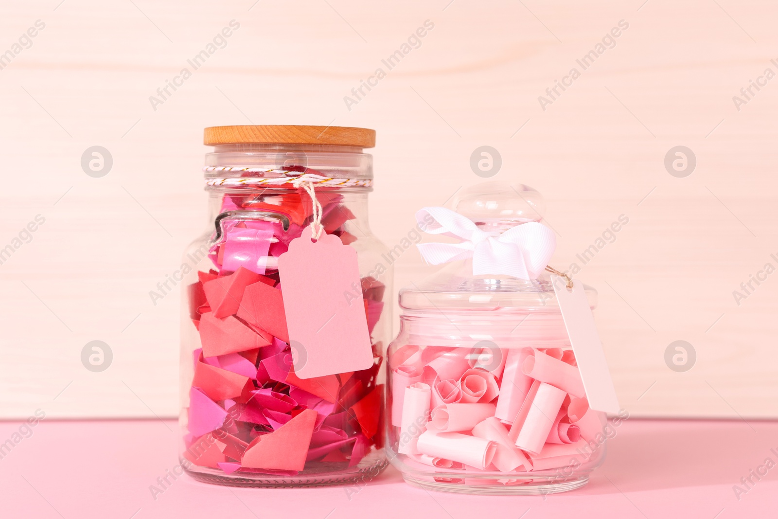 Color paper pieces in glass jars on pink table Photo of Color paper pieces in glass jars on pink table
