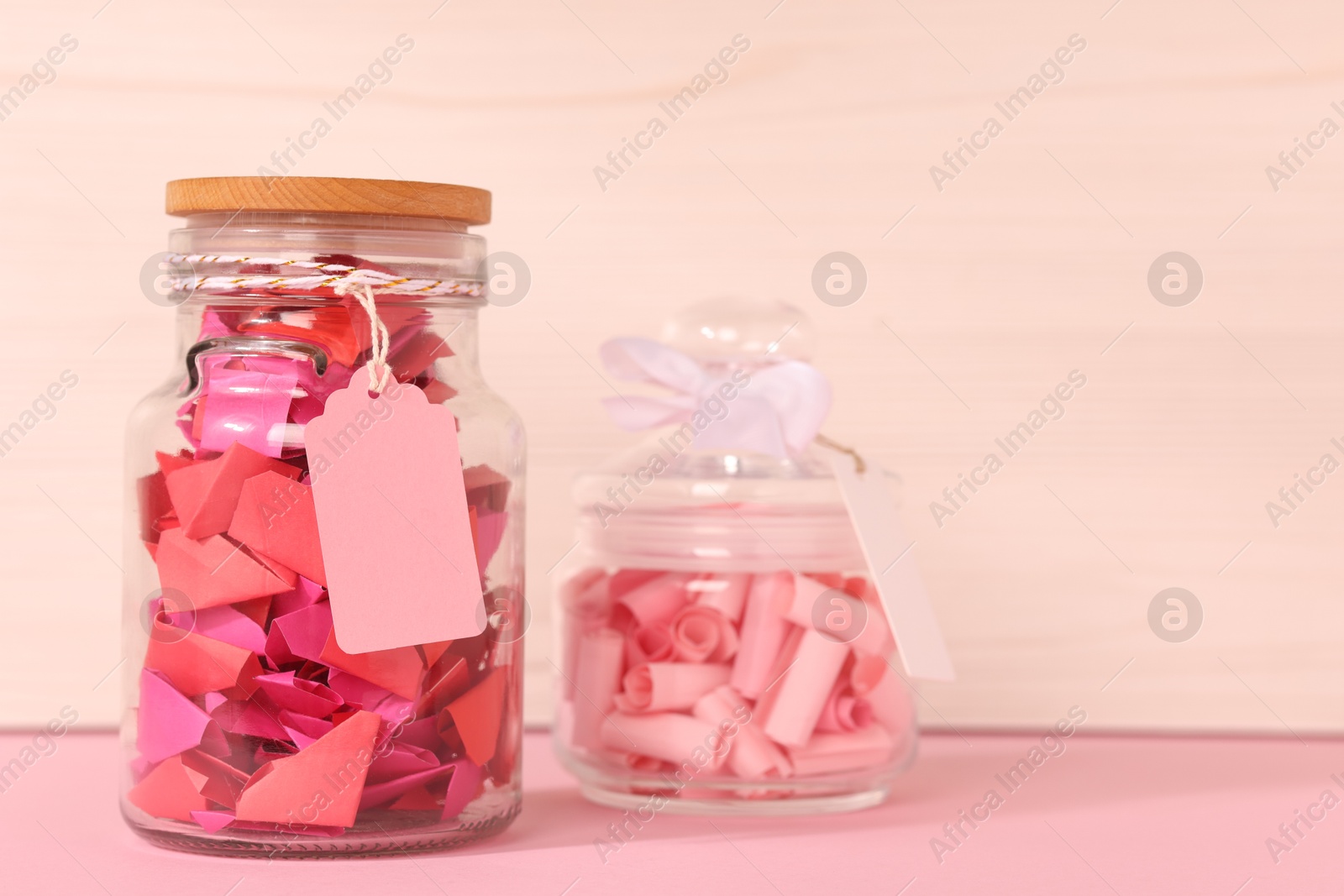 Color paper pieces in glass jars on pink table Photo of Color paper pieces in glass jars on pink table