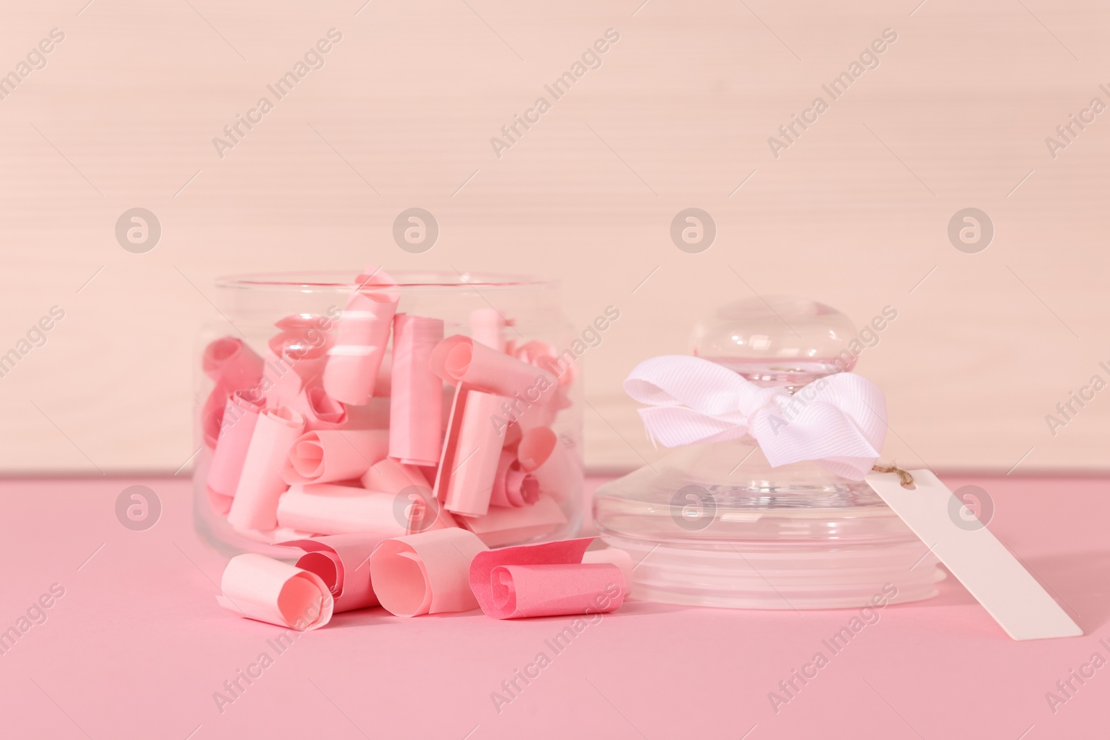 Color paper pieces in glass jar on pink table, closeup Photo of Color paper pieces in glass jar on pink table, closeup