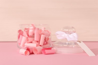 Photo of Color paper pieces in glass jar on pink table, closeup