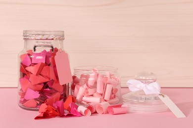 Photo of Color paper pieces in glass jars on pink table