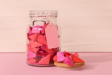 Photo of Color paper pieces in glass jar on pink table