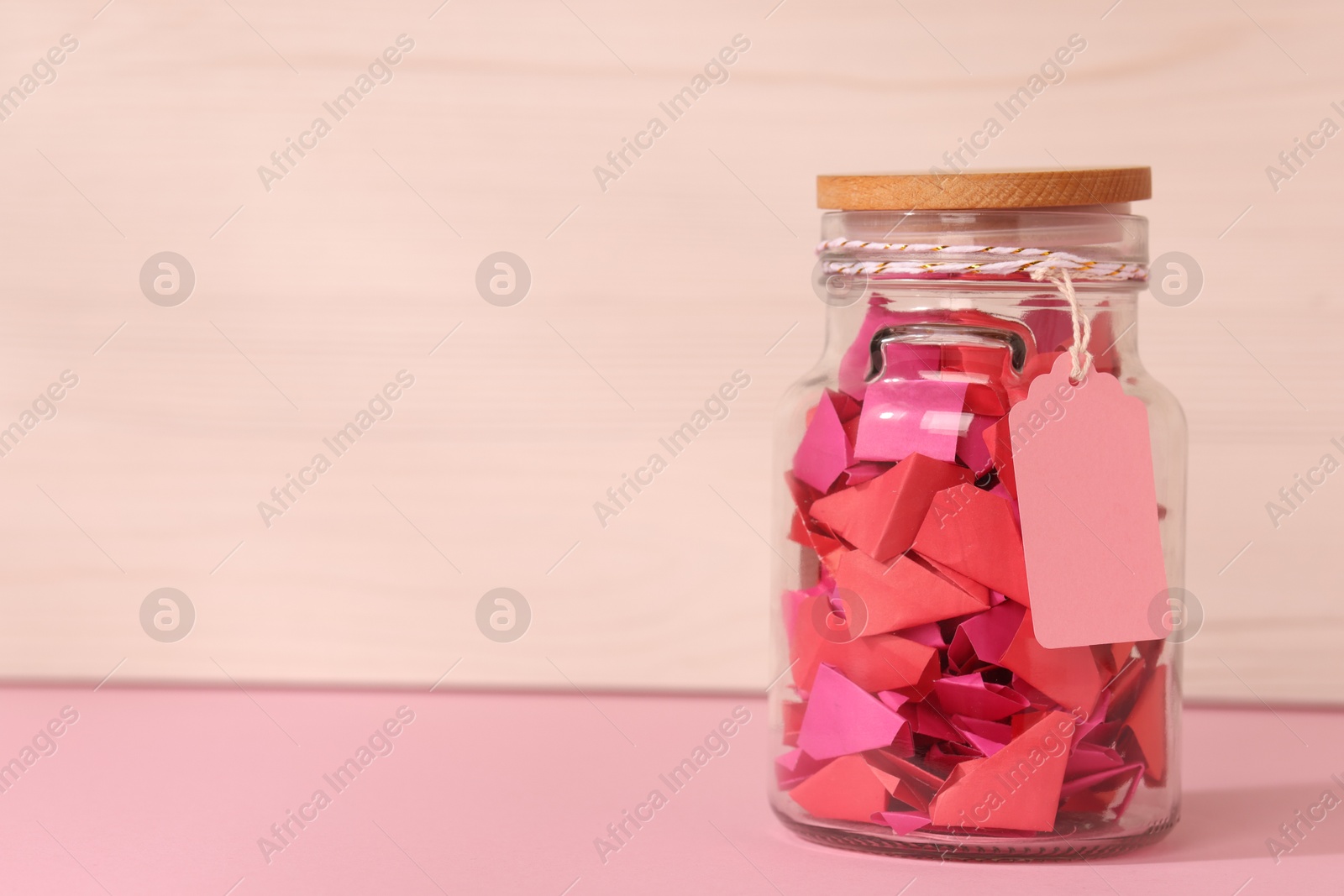 Color paper pieces in glass jar on pink table, space for text Photo of Color paper pieces in glass jar on pink table, space for text