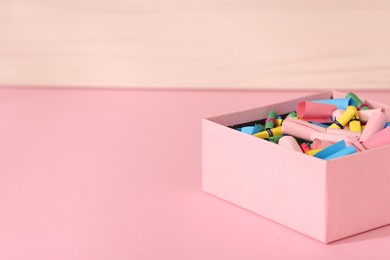 Photo of Color paper pieces in box on pink table, closeup. Space for text