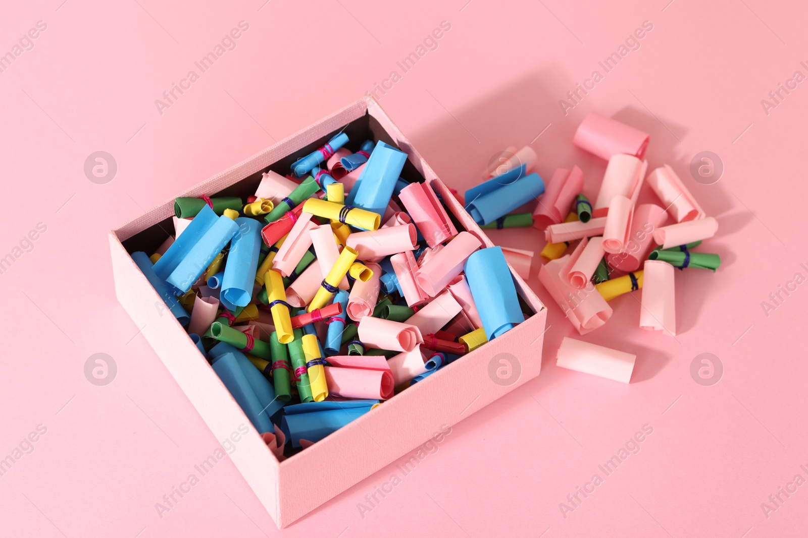 Photo of Color paper pieces in box on pink table, above view