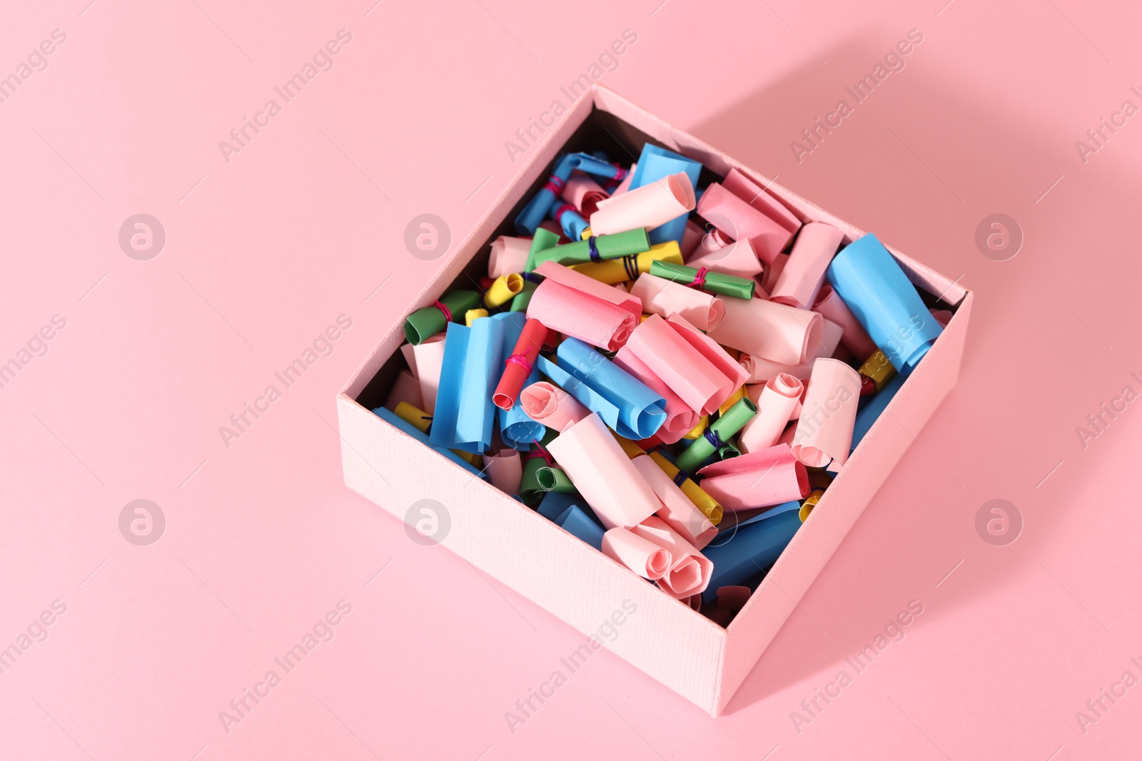 Color paper pieces in box on pink table, above view Photo of Color paper pieces in box on pink table, above view