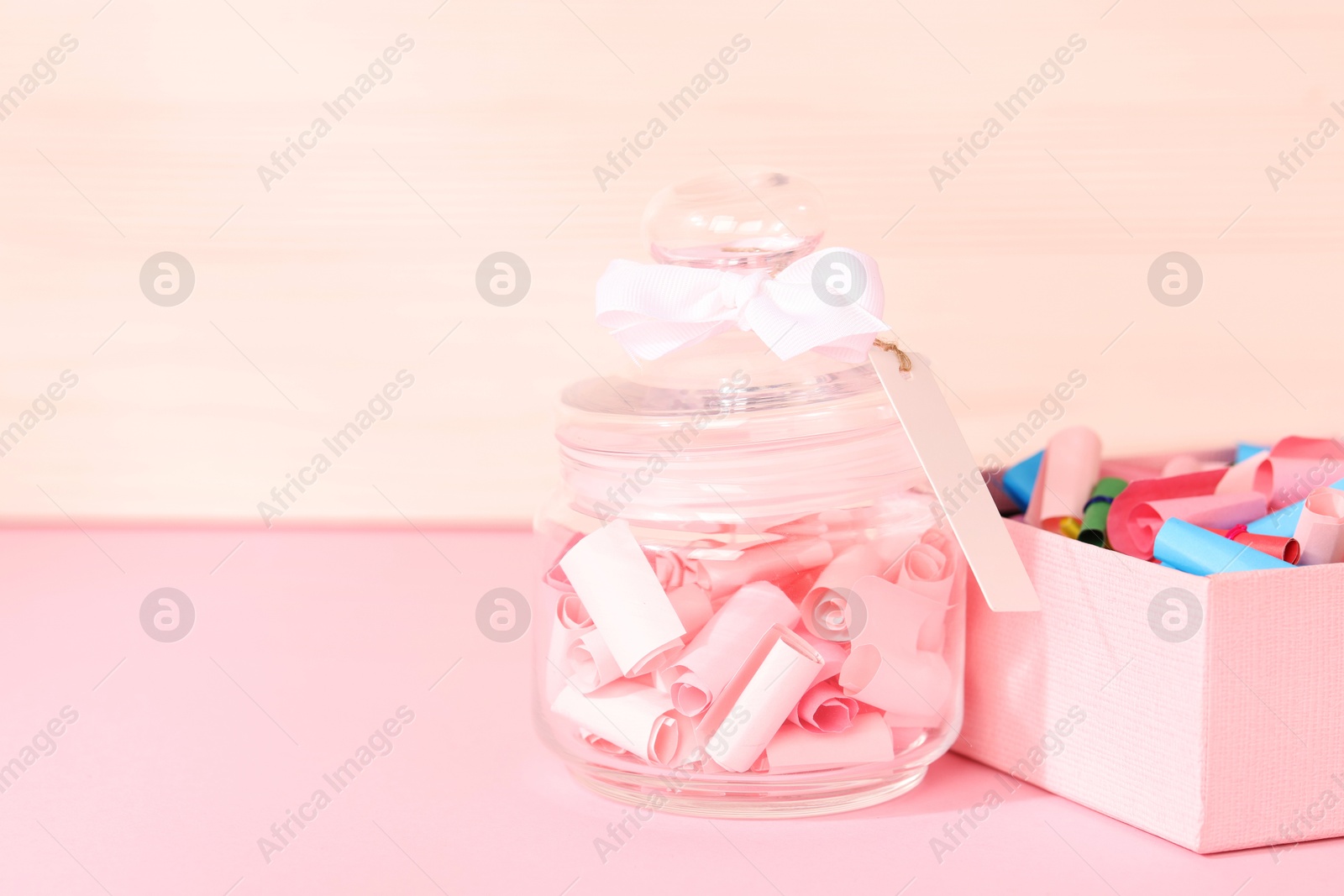 Color paper pieces in box and glass jar on pink table, space for text Photo of Color paper pieces in box and glass jar on pink table, space for text