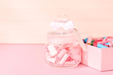 Photo of Color paper pieces in box and glass jar on pink table, space for text