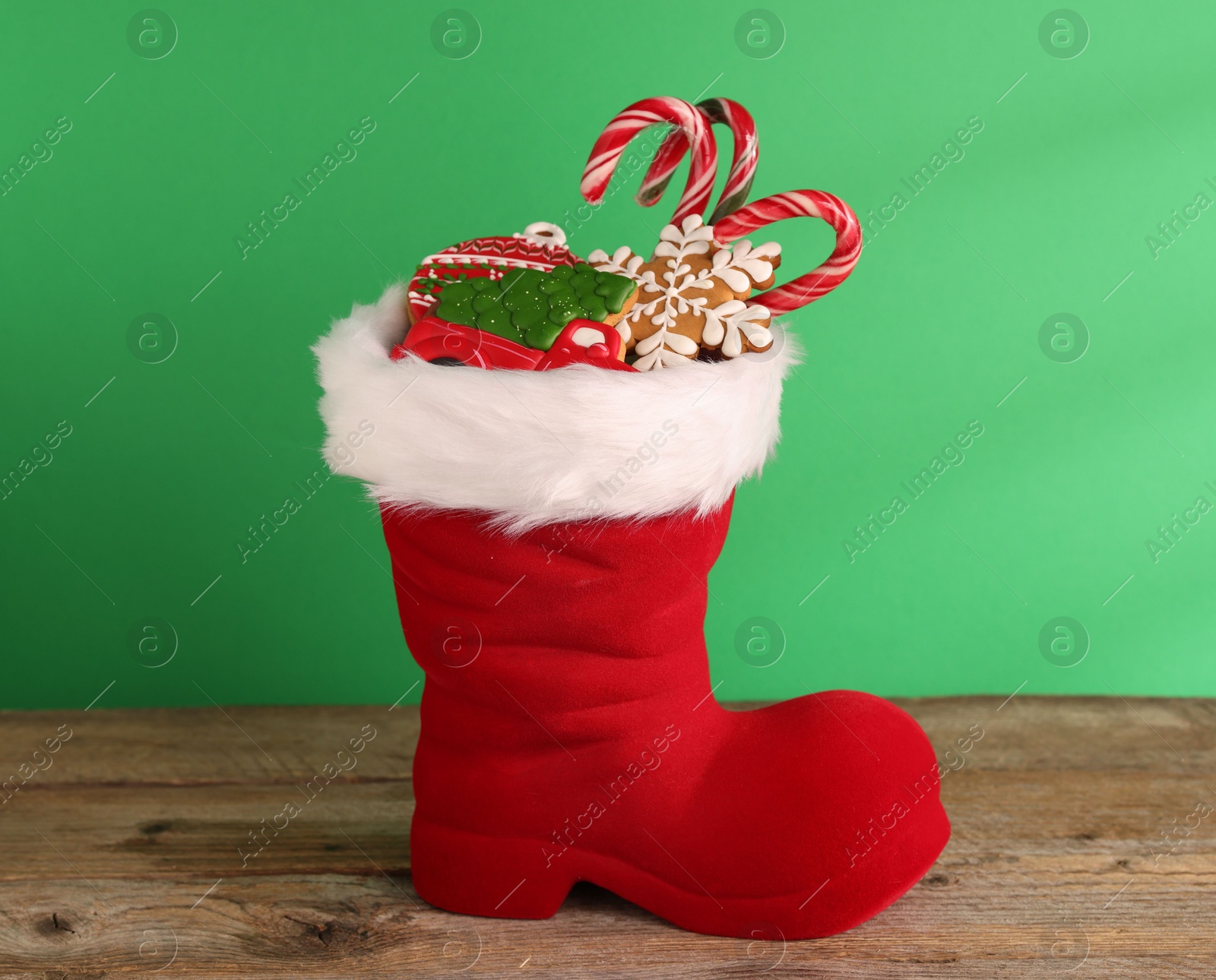 Photo of Saint Nicholas day tradition. Red boot with sweets on wooden table against green background