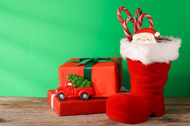 Photo of Saint Nicholas day tradition. Red boot with sweets and gift boxes on wooden table against green background, space for text