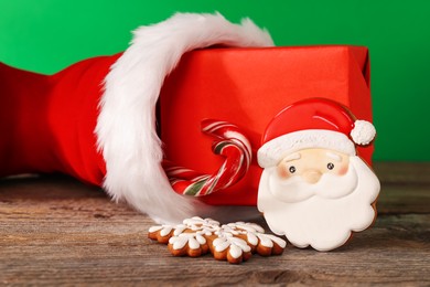 Photo of Saint Nicholas day tradition. Red boot with sweets and gift box on wooden table against green background, closeup