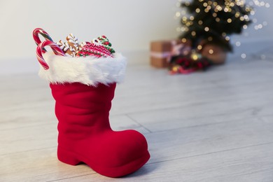 Photo of Saint Nicholas day tradition. Red boot with sweets on floor indoors, space for text