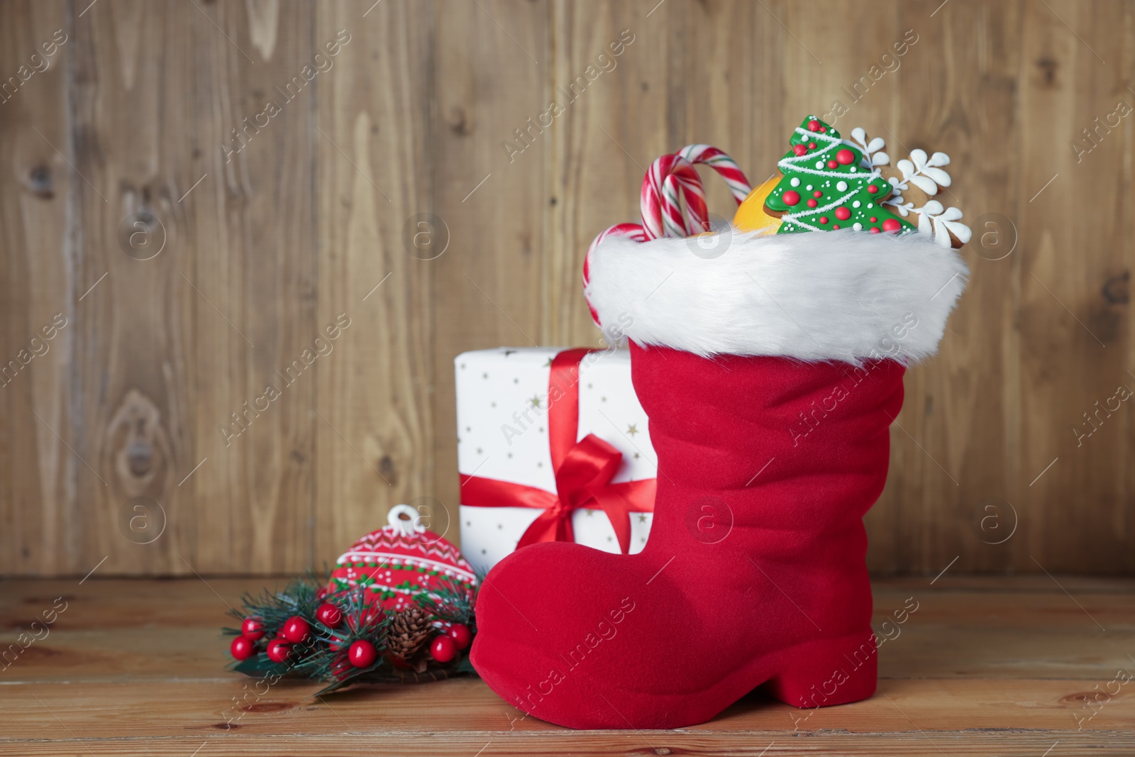 Photo of Saint Nicholas day tradition. Red boot with sweets, gift box and festive decor on wooden table