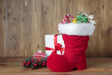 Photo of Saint Nicholas day tradition. Red boot with sweets, gift box and festive decor on wooden table