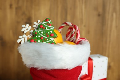 Photo of Saint Nicholas day tradition. Red boot with sweets against wooden background, closeup