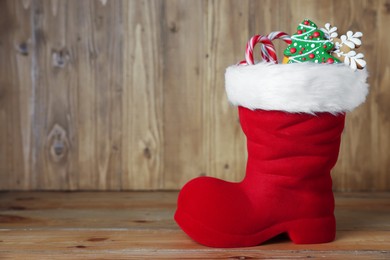 Photo of Saint Nicholas day tradition. Red boot with sweets on wooden table, space for text