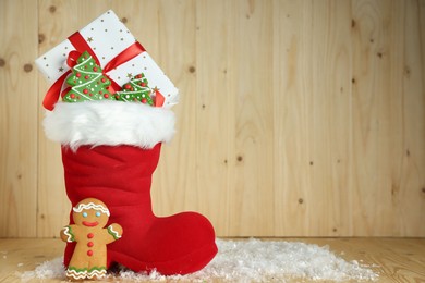 Photo of Saint Nicholas day tradition. Red boot with sweets and gift box on wooden table, space for text