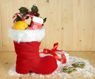 Photo of Saint Nicholas day tradition. Red boot with sweets, festive decor, gift box and artificial snow on wooden table
