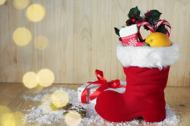 Photo of Saint Nicholas day tradition. Red boot with sweets, festive decor, gift box and artificial snow on wooden table