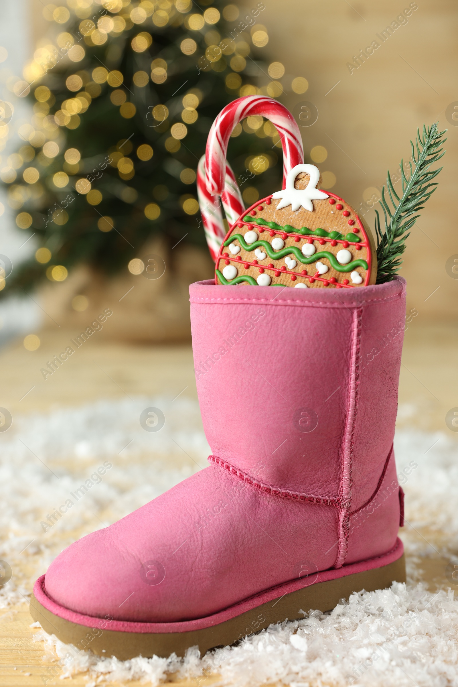 Photo of Saint Nicholas day tradition. Boot with sweets and artificial snow on floor indoors, closeup